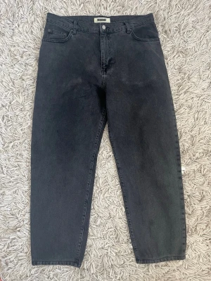 Woodbird Leroy Svart 34/30 - Snygga svarta jeans från Woodbird med rak passform och klassisk femficksdesign. Jeansen har hög midja och är tillverkade i denim med en lätt tvättad look. Perfekta för en avslappnad och trendig stil. Storlek 34/30