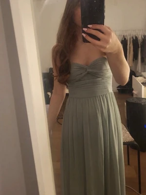 fin balklänning 💗 - Snygg axelbandslös långklänning i ljusgrönt med twistad detalj vid bysten och markerad midja. Klänningen har ett elegant, fallande tyg och är perfekt för speciella tillfällen. Passformen är normal och modellen är klassisk och tidlös.✨