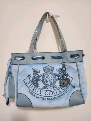 Juicy Couture daydreamer scottie tote  - Superfin ljusblå handväska från Juicy Couture med stora loggan framtill, detaljer i grått konstläder och ett sött hjärtformat hänge med nyckel. Väskan har dubbla handtag, sidoficka och snörningsdetalj upptill. Perfekt för dig som gillar en trendig och lyxig look.