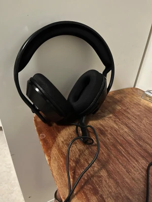 Svarta gaminghörlurar RIG med mic - Säljer ett par svarta over-ear gaminghörlurar från RIG med inbyggd mikrofon och kabelanslutning. Hörlurarna har mjuka öronkuddar och justerbart huvudband i plast och skum för extra komfort. Perfekta för gaming eller videosamtal.