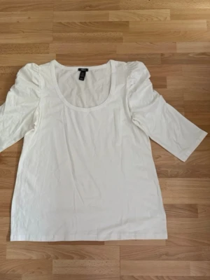 Ny. Vit topp med puffärm från H&M - Säljer en vit topp från H&M med puffade axlar och trekvartsärm. Toppen har rund halsringning och är gjord i mjuk bomull, perfekt för en clean och enkel look. Passar till allt och är superenkel att styla. Bomull.
