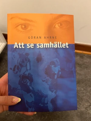 Att se samhället av Göran Ahrne - Kursboken 'Att se samhället' av Göran Ahrne har ett omslag i orange och blått med ett ansikte och siluetter. Perfekt för dig som pluggar sociologi eller samhällsvetenskap. Boken är tryckt på vanligt papper och har mjukt omslag.