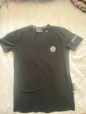 Svart Philipp Plein t-shirt Xl - Snygg svart t-shirt från Philipp Plein med logga på bröstet och diskret märke på ärmen. Klassisk rund halsringning och korta ärmar. Perfekt för dig som gillar exklusiva streetwear-plagg.