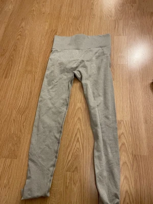 Grå sömlösa leggings med hög midja - Snygga grå leggings med hög midja och sömlös design. Materialet är stretchigt och bekvämt, perfekt för träning eller chill. Diskreta detaljer längs benen och bred linning för extra stöd. Passar dig som gillar stilrena och funktionella plagg.