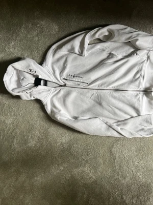 Vit zip-hoodie från Sail Racing Strl M - Snygg vit hoodie med dragkedja från Sail Racing. Klassisk modell med huva, ribbade muddar och logga på bröstet. Perfekt för en clean och sportig look. Tillverkad i mjukt material för extra komfort.