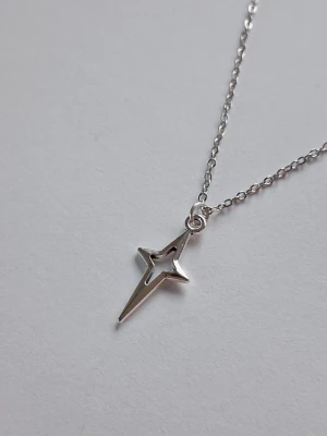 Silverhalsband med stjärnberlock - Snyggt halsband i silverfärg med en unik, spetsig stjärnformad berlock. Kedjan är tunn och stilren, och berlocken har ett modernt, minimalistiskt uttryck Y2K. Perfekt för dig som gillar trendiga accessoarer med en twist. Materialet rostfritt stål. 