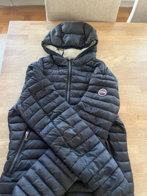 Svart pufferjacka från Colmar - Snygg svart pufferjacka från Colmar med quiltad design och huva. Jackan har dragkedja framtill, två sidofickor med dragkedja och en ljusgrå insida. Perfekt för kalla dagar och riktigt skön att bära.
