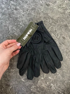 Svarta Roping handskar i syntet - Svarta handskar från Roping med diskret R-logga på ovansidan. Tillverkade i syntetmaterial med elastisk handled för bra passform. Perfekta för dig som gillar stilrena accessoarer och vill ha ett par smidiga handskar.