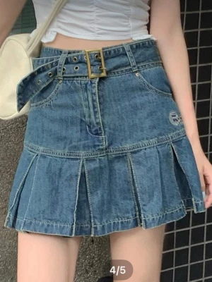 Blå jeanskjol med bälte - Trendig blå jeanskjol från Real Century med markerat bälte i midjan och dekorativa sömmar. Kjolen har fickor fram och ett broderat märke på sidan. Den har en kort, utställd modell med coola detaljer som ger en modern look.