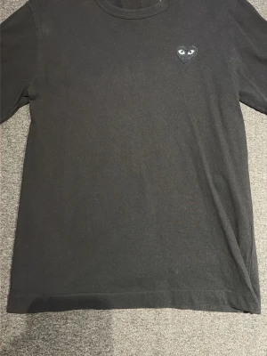 Svart t-shirt Comme des Garçons Play - Svart t-shirt från Comme des Garçons Play med det ikoniska hjärta med ögon broderat på bröstet. Klassisk rund halsringning och korta ärmar. Tillverkad i mjuk bomull som känns skön mot huden.