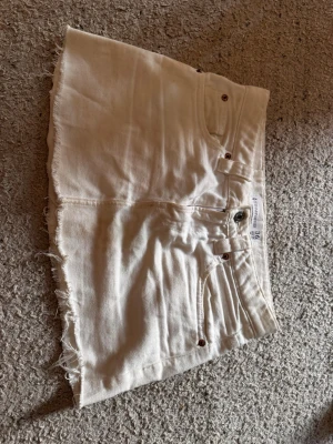 Vit jeanskjol  - Snygg vit jeanskjol från Stradivarius med fyra fickor. Kjolen har klassisk denimlook med bälteshällor och knappstängning framtill. Perfekt för en trendig och avslappnad stil.