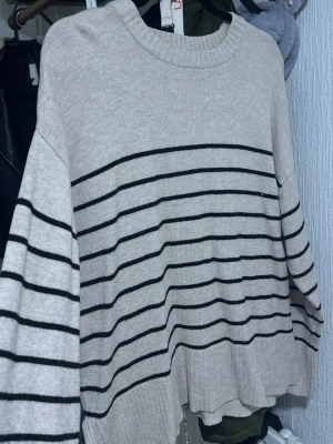 Beige stickad tröja med svarta ränder - Säljer en beige stickad tröja från Lindex med svarta horisontella ränder. Tröjan har rund halsringning, långa ärmar och en avslappnad passform. Perfekt för lager-på-lager och enkel att matcha med jeans eller kjol.
