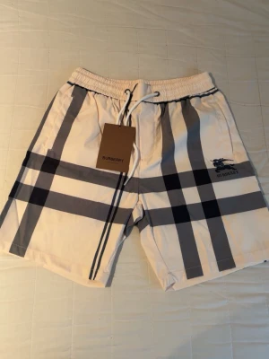 Burberry shorts - Snygga shorts från Burberry i klassiskt beige med svart och grått rutig mönster. Aldrig använda, storlek L passar även M. Pris kan diskuteras!