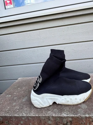 Svarta sock sneakers Acne Studios - Unika svarta sock sneakers med tjock vit sula och stora bokstäver 'A' och 'S' broderade bak på hälen. Skorna har en strumpliknande ovandel i stretchigt tyg och chunky sula för en modern look. Perfekta för dig som vill sticka ut.   