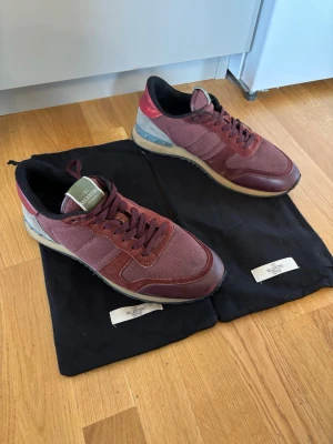 Vinröda Valentino sneakers - Säljer ett par vinröda Valentino sneakers med mesh och läderdetaljer. Skorna har klassisk låg profil, svarta och grå detaljer på hälen samt grönt märke på plösen. 