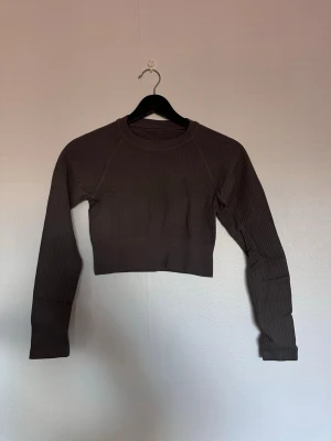 Mörkbrun croppad ribbad långärmad topp - Säljer en mörkbrun croppad långärmad topp från soc. Toppen är ribbad och har en tight passform med rund halsringning. Perfekt för dig som gillar sportiga och trendiga plagg. Diskret soc-logga på ryggen.