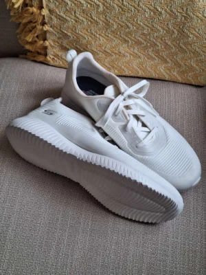 Vita sneakers från Skechers - Stilrena vita sneakers från Skechers med chunky sula och diskret logga på sidan. Skorna har ovandel i textil och syntet, snörning framtill och dragflik bak för enkel påtagning. Perfekta för en clean och modern look.