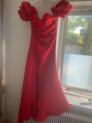 Röd långklänning med puffärmar - Röd långklänning med stora puffärmar och hjärtformad urringning. Klänningen har en elegant, flytande siluett och är tillverkad i ett glansigt material som ger en lyxig känsla. Perfekt för bal eller festligare tillfällen. Хэю