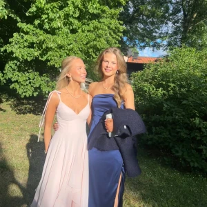 Ljusrosa långklänning med v-ringning - Superfin ljusrosa balklänning med v-ringad front och smala axelband. Klänningen har en flowy kjol och är ärmlös, perfekt för student eller bal. Tillverkad i ett lätt och mjukt material som ger en elegant känsla. Jag är 158 för referens, köpt för ca 2500 och endast använd en gång!! Fodral tillkommer