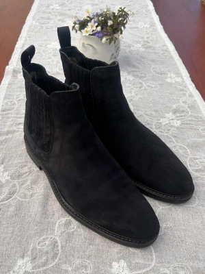 Fur Lined Chelsea boots från Rose & Born - Stilrena mörkblåa Chelsea boots i mocka från Rose & Born. Klassisk siluett med resår på sidorna och dragflikar både fram och bak. Skorna är fodrade med päls, vilket ger än väldigt skön känsla på foten. Perfekta för dig som vill ha en tidlös och snygg look till hösten och vintern.