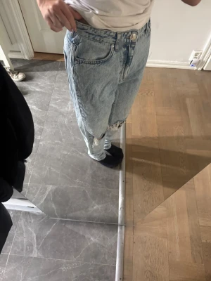Ljusa baggy jeans med slitningar - Säljer ett par ljusa baggy jeans med slitningar på knäna. Jeansen har hög midja, klassiska fem fickor och är gjorda i denim. Perfekt för dig som gillar en avslappnad och trendig look.