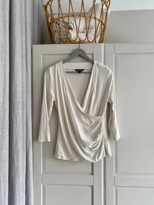 Vit omlottopp Lauren Ralph Lauren - Snygg vit omlottopp från Lauren Ralph Lauren med v-ringning och trekvartsärm. Toppen har en draperad omlottdesign framtill och sitter jättesnyggt på. Nypris 999 kr. 