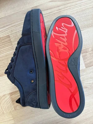 Marinblå loubs  sneakers - Snygga marinblå sneakers från Christian Loubs i mocka med klassisk röd sula och diskret logga på sidan. Skorna har svarta skosnören och en låg silhuett som ger en clean och exklusiv look. Tillverkade i Italien.