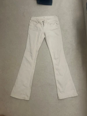 Vita bootcut jeans med låg midja - Snygga vita bootcut jeans med låg midja och klassisk femficksdesign. Jeansen har utsvängda ben och stängs med dragkedja och knapp. Perfekta för dig som gillar en retrostil och vill sticka ut med ljusa byxor. Materialet är bomull med lite stretch för extra komfort.