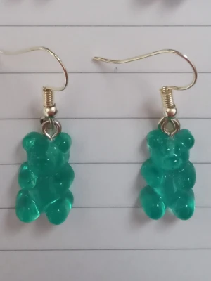 Turkosa björn örhängen  - Säljer ett par unika örhängen med turkos gummibjörns-hängen i plast. Örhängena har krokar i metall och är knappt använda. 