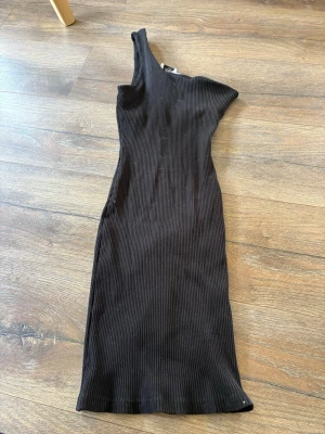 Svart oneshoulder klänning NA-KD - Säljer en svart ribbad oneshoulder klänning från NA-KD x Iva Nikolina. Klänningen är figurnära och lite stretchig 