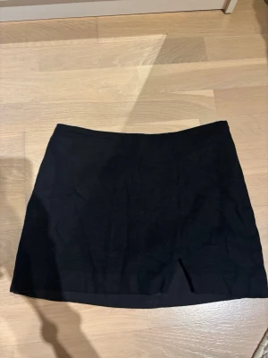 Svart minikjol från Divided - En svart minikjol från Divided, H&M med rak passform och liten slits framtill. Kjolen har dragkedja i sidan och är i linne. Perfekt för att skapa en stilren och trendig look. Knappt använd 