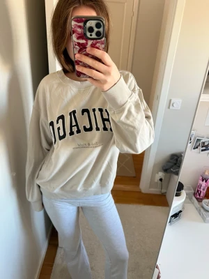 Beige sweatshirt med CHICAGO-tryck - Säljer en oversized beige sweatshirt med CHICAGO-tryck på bröstet. Tröjan har rund halsringning, långa ärmar och ribbade muddar vid ärmslut och nederkant. Perfekt för en avslappnad och trendig look. Finns några fläckar längst ner (se bild) men inget som syns vid användning