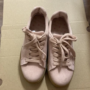 Ljusrosa sneakers med mockakänsla - Snygga ljusrosa sneakers med klassisk låg profil och breda skosnören. Ovandelen har en mockaliknande yta och innersulan är dekorerad med små stjärnor. Yttersulan är ljusbrun och ger en fräsch kontrast till skon. De är som nya har använt bara två gånger. 