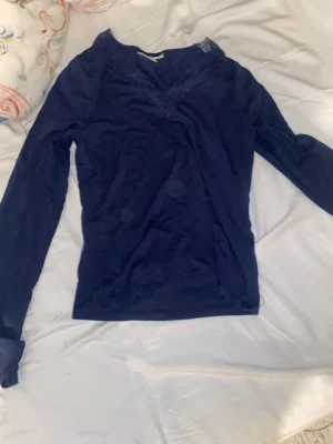Mörkblå långärmad topp Gina Tricot - Mörkblå långärmad topp från Gina Tricot med v-ringning och spetsdetaljer vid halsen. Topp i mjukt material som sitter snyggt och passar perfekt till jeans eller kjol. Enkel men ändå med en fin touch av spets vid urringningen.