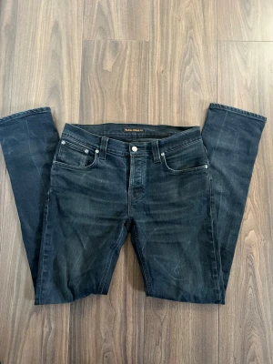 Mörkblå jeans från Nudie Jeans 32 W 34 L - Snygga mörkblå jeans från Nudie Jeans med klassisk femficksdesign och raka ben. Jeansen har subtila slitningar och kontrastsömmar, samt en liten logotyp på bakfickan. Perfekta för en avslappnad och trendig look grim tim modell.