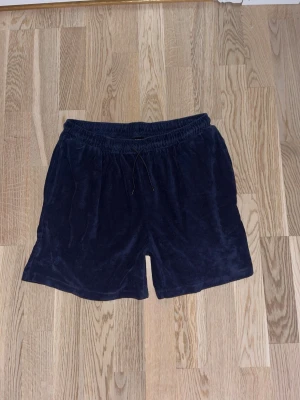 Mörkblå shorts från Reaction - Mörkblå shorts från Reaction i mjukt frottématerial. De har elastisk midja med snörning för skön passform och en avslappnad, loose siluett. Perfekta för varma dagar eller chill hemma.