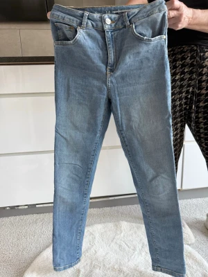 Ljusblå skinny jeans från Never Denim - Säljer ett par ljusblå skinny jeans från Topshop med klassisk femficksdesign och hög midja. Jeansen har gul kontrastsöm och knapp med logga. Perfekta för en avslappnad och trendig look.