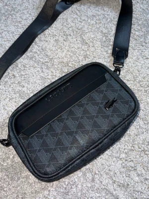 Lacoste Väska Oanvänd  - Säljer min Lacoste väska som jag fick i present men är tyvärr inte min stil så den har knappast använts. Den är i mycket bra skick..
