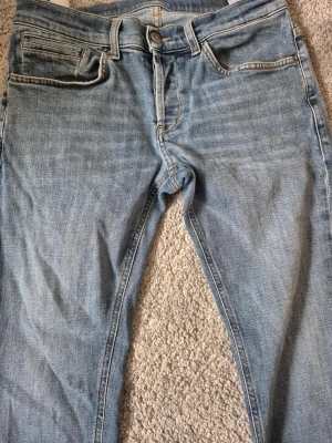 Ljusblå raka jeans från Dondup - Säljer ett par ljusblå jeans från Dondup med klassisk femficksmodell och raka ben. Jeansen har orangea sömmar och en diskret logga på bakfickan. Tillverkade i mjuk denim som ger en avslappnad look. Stl 32