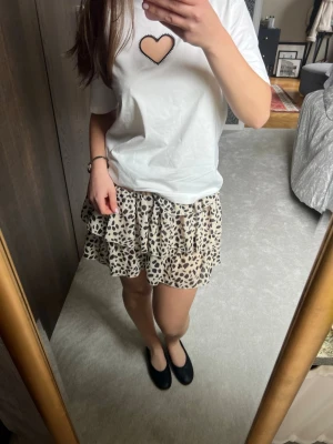 Beige leopardmönstrad volangkjol - Supersöt kort kjol med volanger och leopardmönster/prickar i beige och svart. Kjolen har en glittrig resår i midjan som ger en snygg detalj. Perfekt för dig som gillar trendiga och lekfulla plagg.