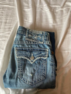 True Religion ljusblå bootcut jeans - Säljer ett par ljusblå bootcut jeans från True Religion med ikoniska kontrastsömmar och snygga fickdetaljer. Storlek 31, seat 34. Jeansen har klassisk femficksdesign och är tillverkade i denim med cool faded effekt. Säljer dom på grund av att jag är desperat för pengar till sommaren och att jag bytt still och inte längre använder dom.👌👌💯💯👍👍🔛🔝