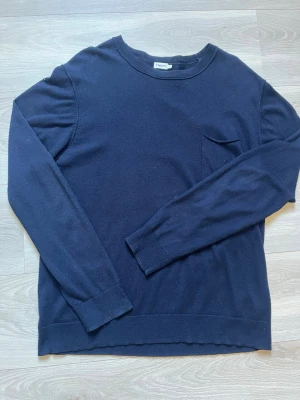 Mörkblå stickad tröja Filippa K - Mörkblå stickad tröja från Filippa K med rund halsringning och en liten bröstficka. Tröjan har långa ärmar och ribbade muddar vid ärmslut och nederkant. Enkel och stilren design som passar till mycket. Storlek XL men sitter som L!