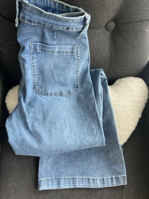 Ljusblå jeans med knappar framtill - Säljer ett par ljusblå jeans med utsvängda ben och flera snygga silverfärgade knappar framtill. Jeansen har en klassisk femficksmodell och är gjorda i mjukt denimtyg som är elastisk. Perfekta för en avslappnad och trendig look. Har kostat 999kr, inköpta på Two Angels , Vallgatan . 