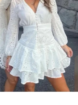 Vit kortklänning med volang - Superfin vit kortklänning från Fashion Nova, v-ringning och knappar framtill. Klänningen har långa ärmar, markerad midja och dubbla volanglager i kjolen. Perfekt till studenten!