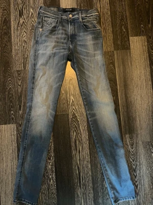 Blå slim fit jeans från Replay - Snygga blå slim fit jeans från Replay med slitningar och tvättade detaljer. Klassisk femficksmodell med dragkedja och knapp. Bakfickorna har dekorativa sömmar och läderpatch i midjan. Perfekta för en avslappnad och trendig look.