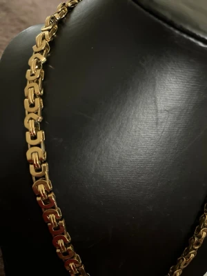Guldfärgat kedjehalsband - Snyggt halsband i guldfärg med kraftiga, rektangulära länkar som ger en modern och stilren look. Halsbandet har en glänsande finish och passar perfekt för dig som vill sticka ut med accessoarerna. Märke och material är ej angivet.