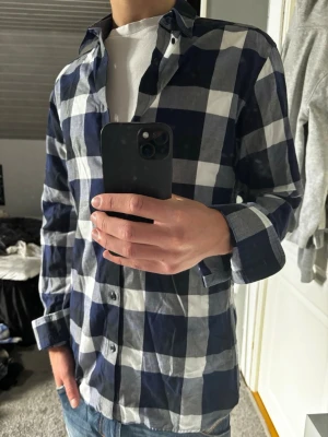Blåvitrutig skjorta - Säljer en blå och vit rutig skjorta i bomull. Skjortan har klassisk krage, knappar framtill och långa ärmar. Perfekt för dig som gillar en avslappnad men ändå stilren look.