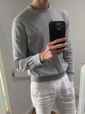 Grå tröja från Polo Ralph Lauren - Snygg grå sweatshirt från Polo Ralph Lauren med rund halsringning och diskret broderad logga på bröstet. Tröjan har ribbade muddar vid ärmslut och nederkant, perfekt för en clean och avslappnad stil. Tillverkad i mjukt bomullsmaterial.