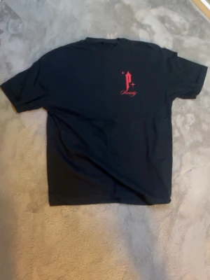 Svart Paranoid Society t-shirt - Svart t-shirt från Paranoid Society med tryck fram och bak. På bröstet finns ett rött P och texten Society, medan ryggen har en stor vit duva, röd text och grafiskt tryck. T-shirten har normal passform och är kortärmad, tillverkad i bomull.