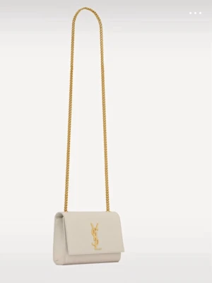 Vit axelväska från Saint Laurent - Säljer en snygg vit axelväska från Saint Laurent med guldfärgad kedjerem och ikoniska YSL-loggan framtill. Väskan har en stilren, rektangulär form och är tillverkad i slätt läder. Perfekt för dig som vill ha en lyxig och trendig accessoar.